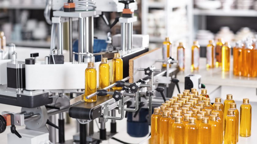 Horizontal shot of cosmetics or pharmacy plant with automated equipment. Transparent plastic bottles filled with yellow substance standing on desk and conveyor line, ready for transportation
